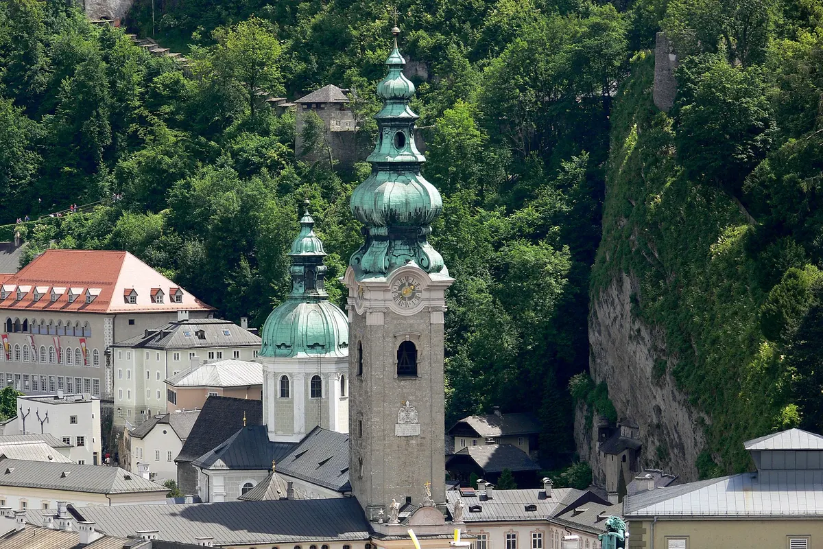 The green copper-roofed tower and dome of St. Peter's abbey church in Salzburg, with the wooded Mönchsberg rising behind it.