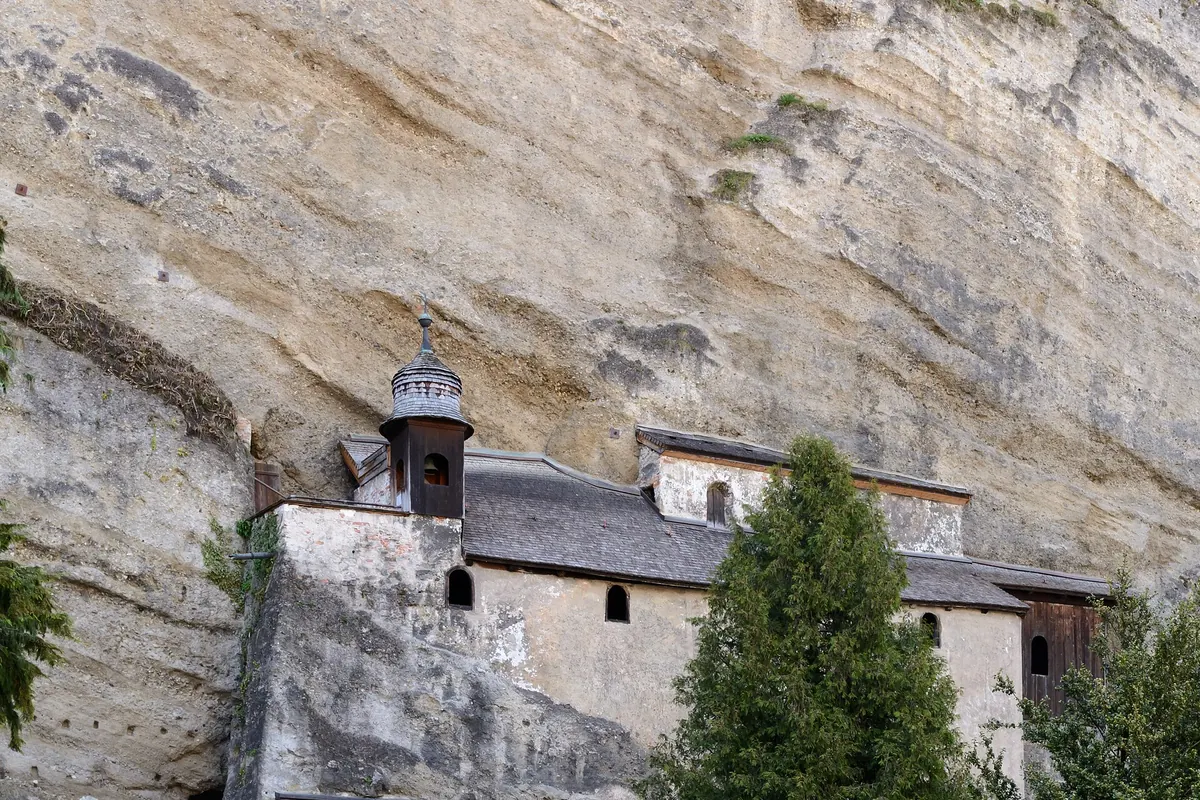 A cemetery of ornate wrought-iron grave crosses below a sandstone cliff, with a small chapel built against the rock.