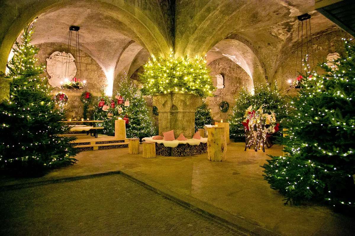 A vaulted rock-cut cellar room of the Stiftskeller hung with Christmas trees and lights.