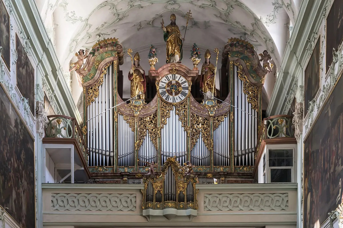 A gilded organ case with silver pipes and a clock inside the white-and-gold Rococo nave of St. Peter's abbey church.